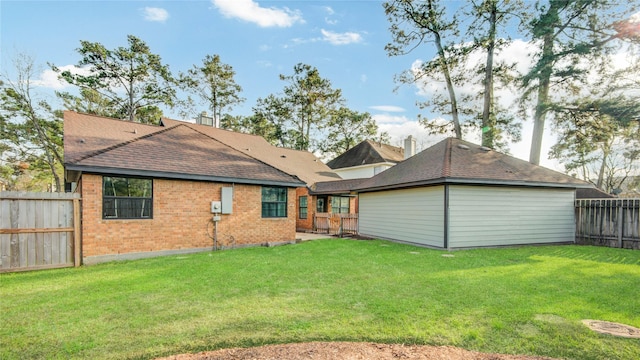 back of house featuring a fenced backyard, a yard, roof with shingles, and brick siding