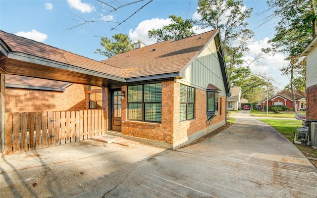 back of house featuring brick siding, a chimney, and roof with shingles