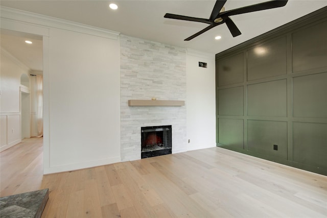 unfurnished living room featuring ceiling fan, ornamental molding, light wood-style floors, and a decorative wall