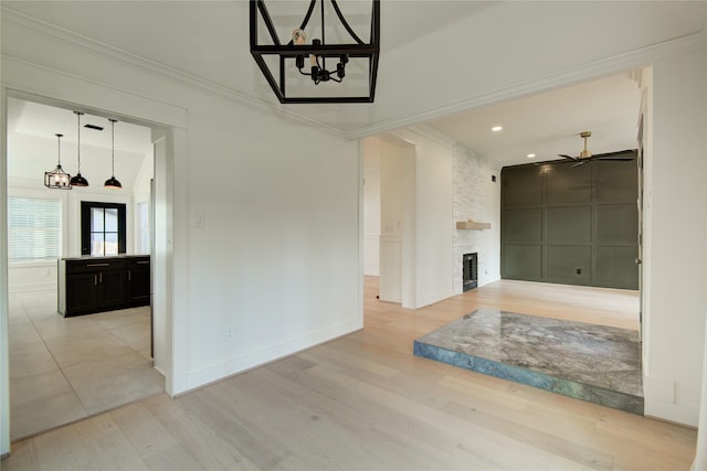 unfurnished living room featuring baseboards, ornamental molding, light wood-style flooring, and ceiling fan with notable chandelier