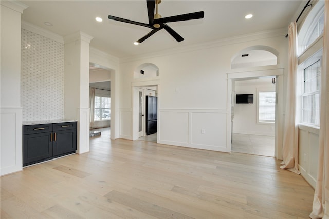 unfurnished living room featuring ornamental molding, a decorative wall, ceiling fan, and a wealth of natural light