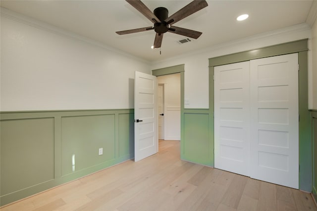 unfurnished bedroom featuring visible vents, ornamental molding, light wood-style flooring, and a decorative wall
