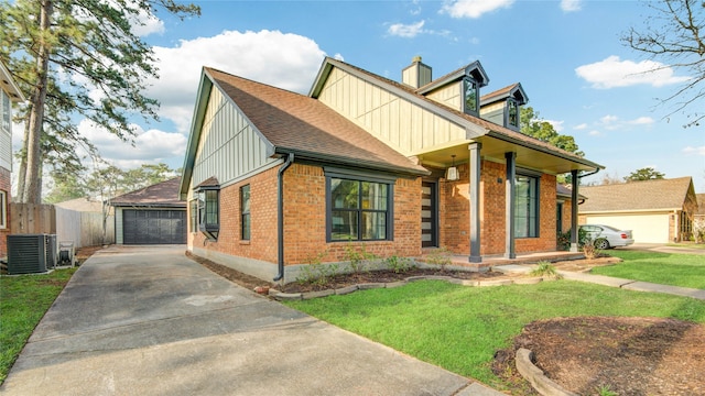 new england style home with board and batten siding, roof with shingles, central AC unit, a detached garage, and brick siding