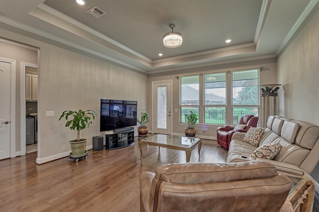 living room with visible vents, hardwood / wood-style flooring, baseboards, ornamental molding, and a tray ceiling