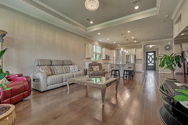 living room featuring ornamental molding, a tray ceiling, dark wood finished floors, and visible vents