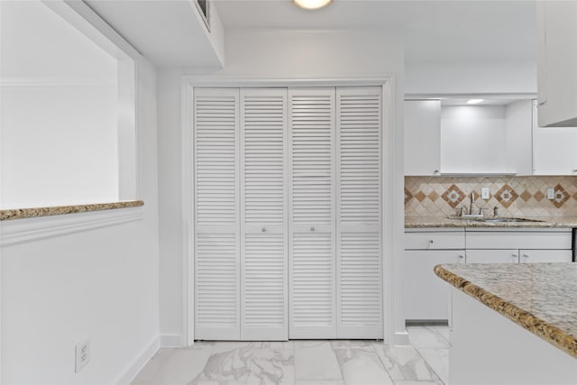 kitchen with a sink, white cabinetry, marble finish floor, and tasteful backsplash