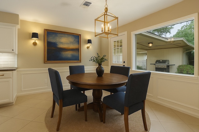 dining area with light tile patterned flooring, a decorative wall, a chandelier, and a wainscoted wall