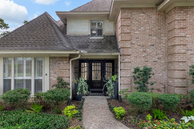 entrance to property featuring a shingled roof and brick siding