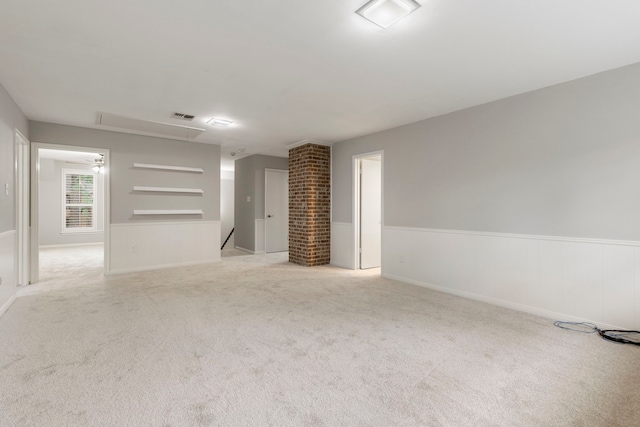 unfurnished living room with attic access, light carpet, and wainscoting