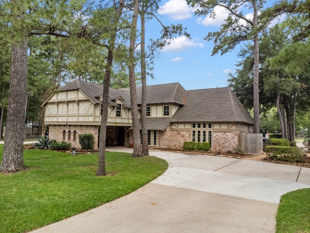 english style home with curved driveway, brick siding, a front lawn, roof with shingles, and stucco siding