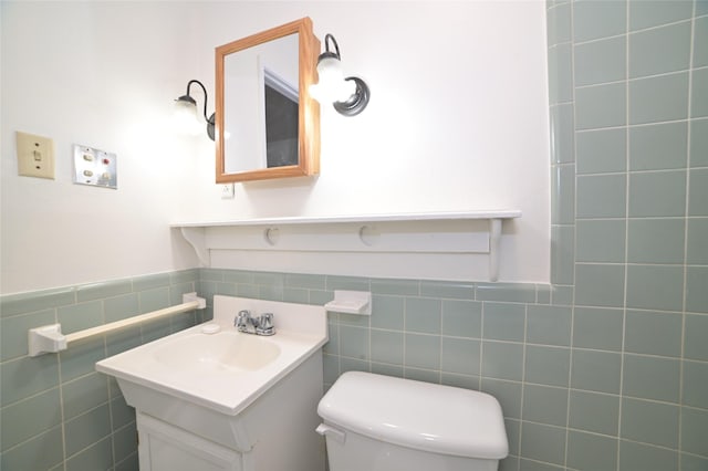 bathroom featuring vanity, wainscoting, toilet, and tile walls