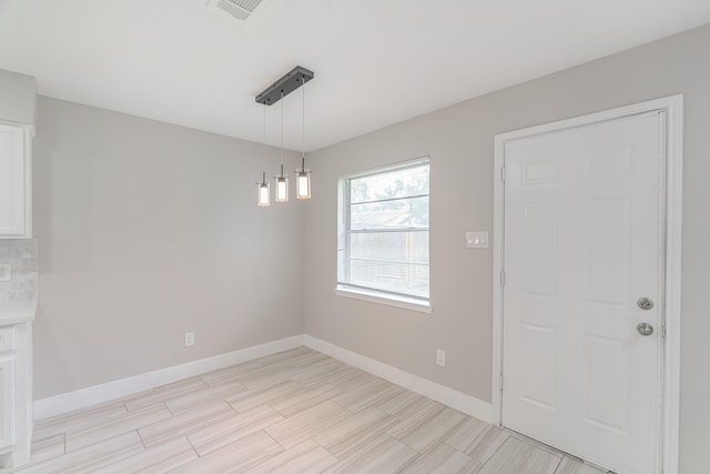 unfurnished dining area featuring baseboards, light wood finished floors, and visible vents