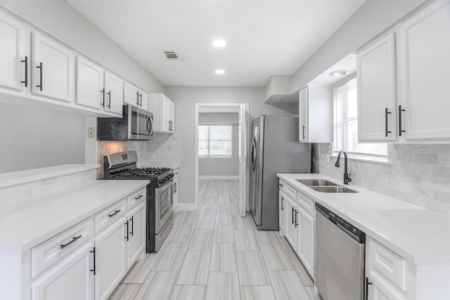 kitchen featuring baseboards, white cabinets, a sink, appliances with stainless steel finishes, and backsplash