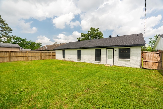 rear view of house with a fenced backyard, a lawn, roof with shingles, and brick siding