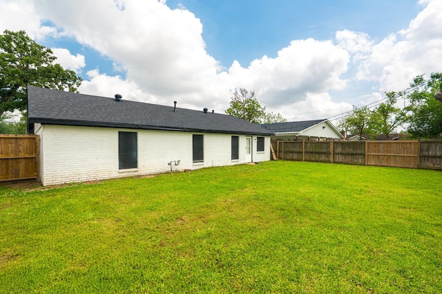 back of house featuring a lawn, a fenced backyard, roof with shingles, and brick siding
