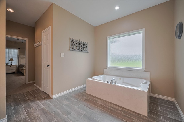 ensuite bathroom featuring baseboards, wood finish floors, ensuite bath, and a bath