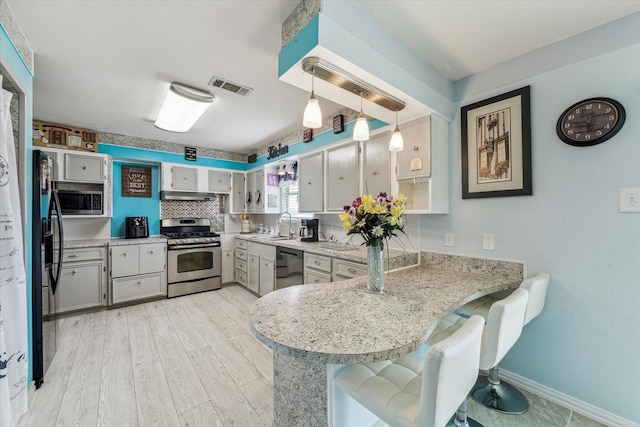 kitchen featuring appliances with stainless steel finishes, a sink, a peninsula, under cabinet range hood, and visible vents