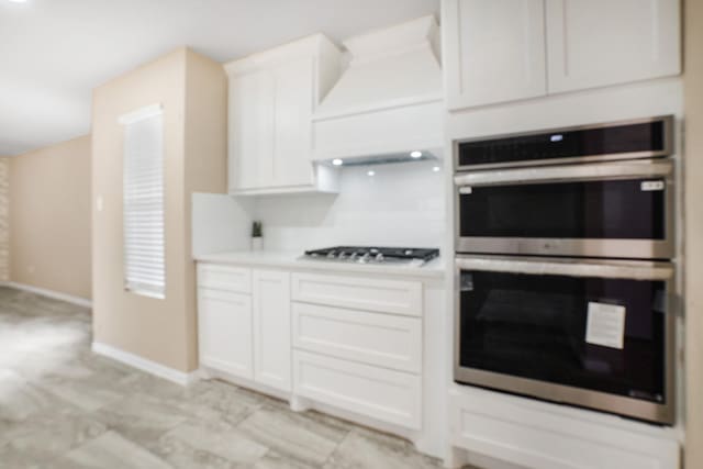 kitchen featuring stainless steel double oven, premium range hood, white cabinetry, baseboards, and gas stovetop