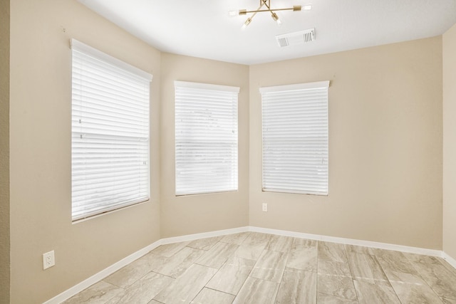spare room with a notable chandelier, visible vents, a healthy amount of sunlight, and marble finish floor
