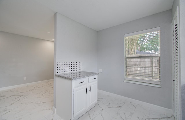 kitchen with light stone counters, marble finish floor, baseboards, and white cabinets