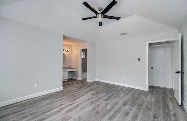 unfurnished bedroom with visible vents, lofted ceiling, wood finished floors, baseboards, and connected bathroom