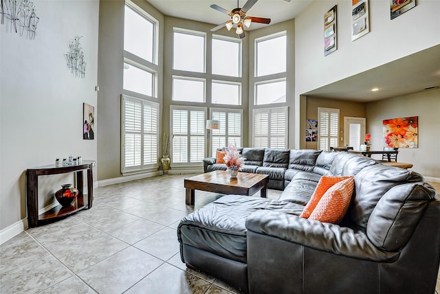 living area featuring light tile patterned floors, baseboards, a ceiling fan, and a towering ceiling