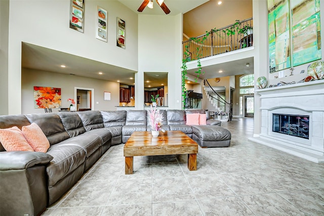 living room with stairs, a ceiling fan, a glass covered fireplace, and a towering ceiling