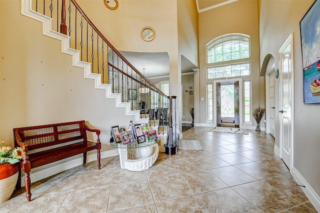 tiled entrance foyer with stairs, baseboards, ornamental molding, and a towering ceiling