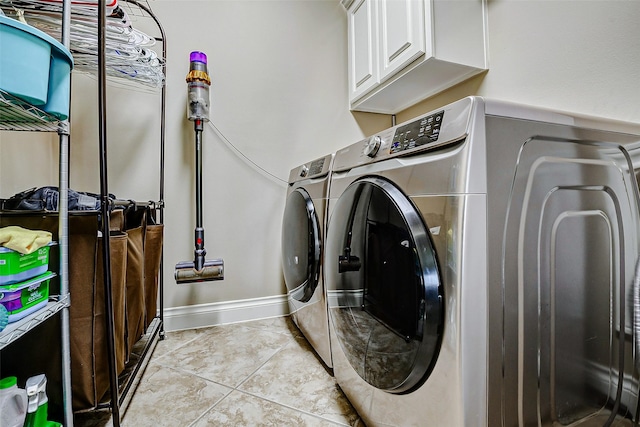 laundry room with washing machine and clothes dryer, baseboards, light tile patterned floors, and cabinet space