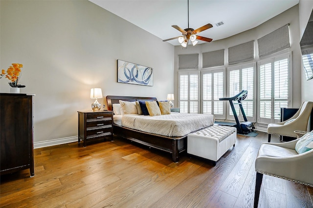 bedroom with a ceiling fan, a towering ceiling, visible vents, hardwood / wood-style flooring, and baseboards