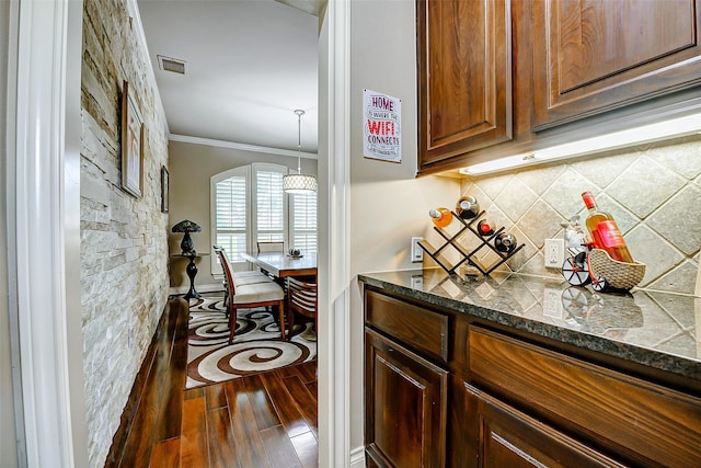 kitchen featuring visible vents, ornamental molding, dark wood-type flooring, dark stone countertops, and backsplash