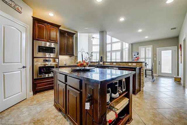 kitchen featuring ceiling fan, appliances with stainless steel finishes, a center island, decorative backsplash, and visible vents