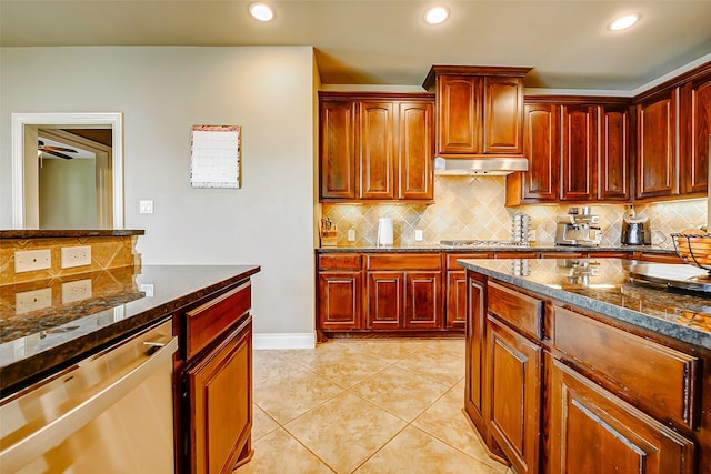 kitchen with under cabinet range hood, stainless steel appliances, dark stone counters, and reddish brown cabinets