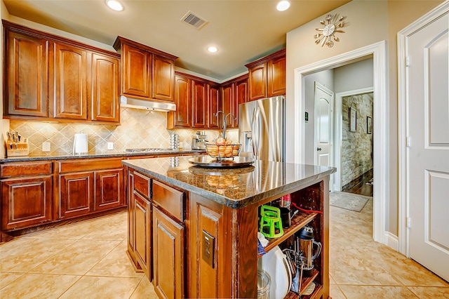 kitchen featuring visible vents, under cabinet range hood, dark stone countertops, backsplash, and stainless steel appliances