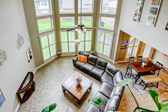 living area featuring baseboards, tile patterned floors, ceiling fan, and a towering ceiling