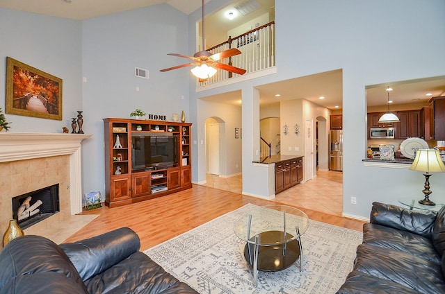 living area with visible vents, a towering ceiling, ceiling fan, light wood-type flooring, and arched walkways