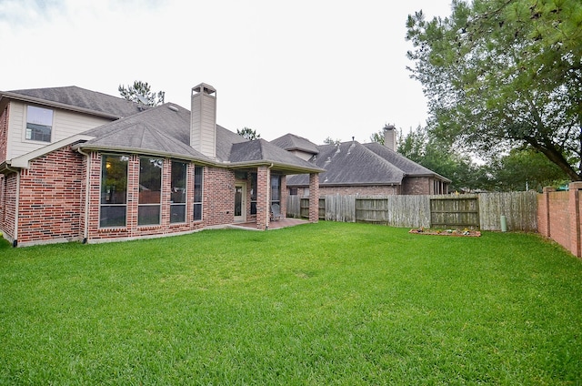 back of house featuring a chimney, a lawn, a patio area, brick siding, and a fenced backyard