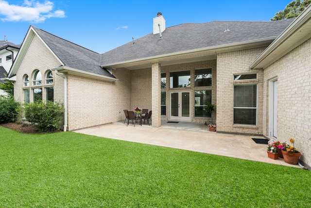 rear view of property with roof with shingles, brick siding, french doors, a lawn, and a patio