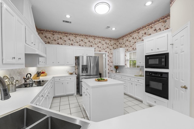 kitchen with visible vents, a center island, black appliances, under cabinet range hood, and wallpapered walls