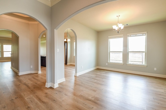 empty room with visible vents, baseboards, a chandelier, arched walkways, and light wood-style flooring