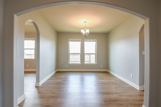 empty room featuring light wood-style floors, arched walkways, a notable chandelier, and a wealth of natural light