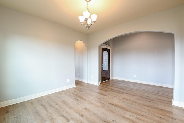 empty room with baseboards, arched walkways, light wood finished floors, and a chandelier