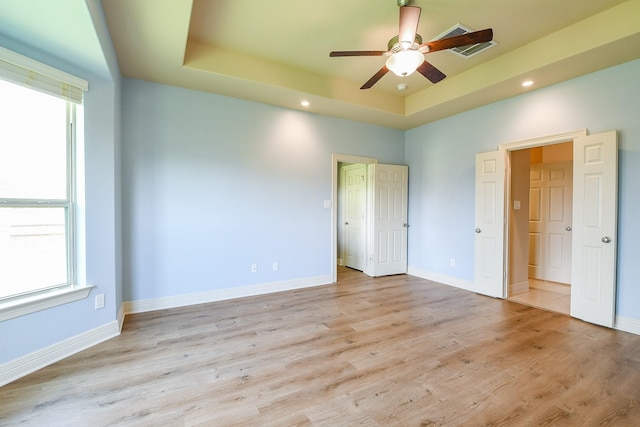 unfurnished bedroom featuring recessed lighting, light wood-style flooring, baseboards, and a tray ceiling