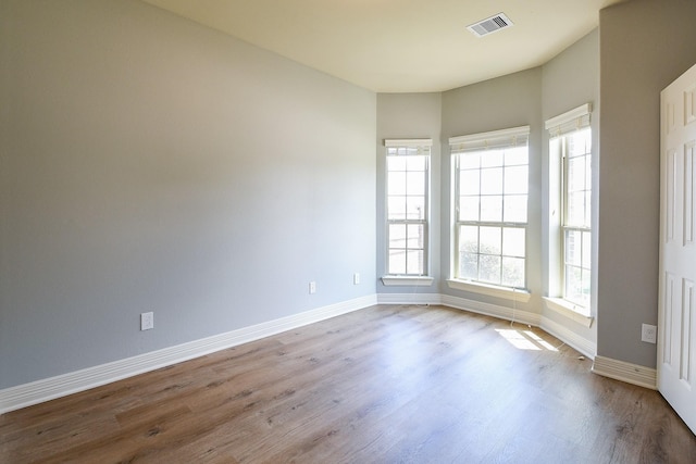 unfurnished room featuring baseboards, visible vents, and wood finished floors