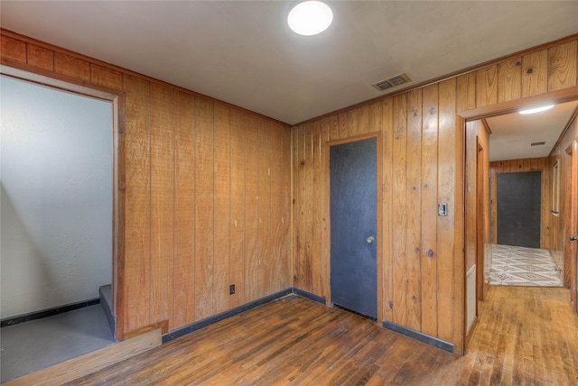 spare room with baseboards, wood walls, wood finished floors, and visible vents