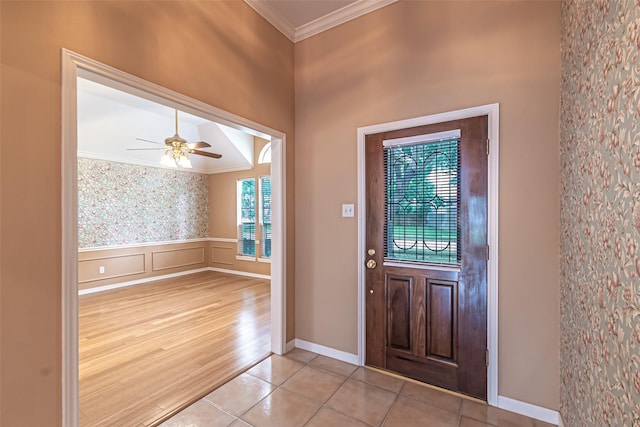 entrance foyer featuring crown molding, ceiling fan, a wainscoted wall, baseboards, and light tile patterned floors