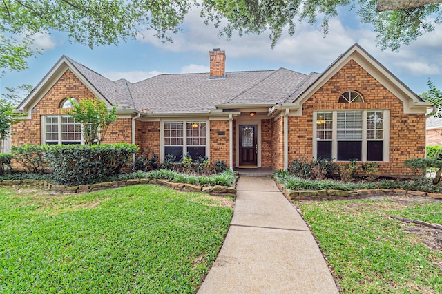 ranch-style home with a chimney, a shingled roof, and a front yard