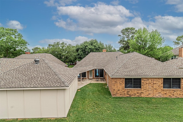 back of house with a shingled roof, brick siding, a chimney, a patio, and a yard