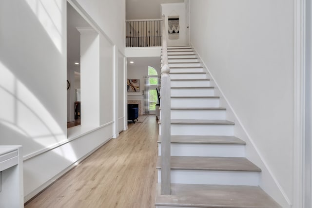 staircase featuring a fireplace, wood finished floors, and a towering ceiling