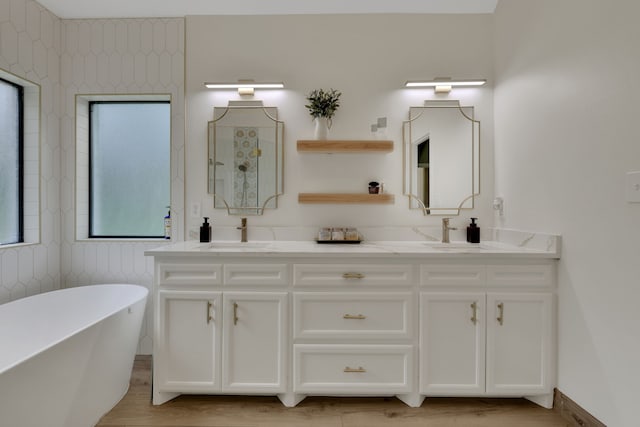 full bathroom with double vanity, a sink, a freestanding bath, and wood finished floors